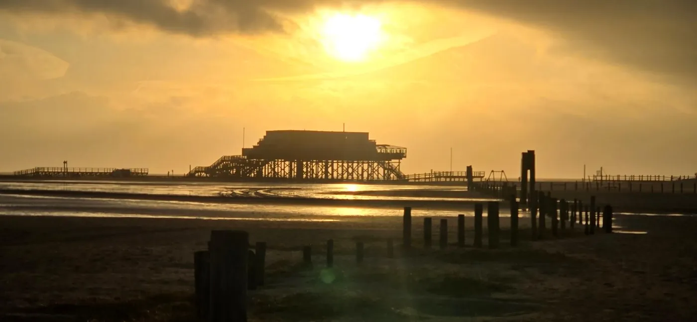 Pfahlbau am Strand von St. Peter-Ording als Silhouette vor tiefstehender Sonne